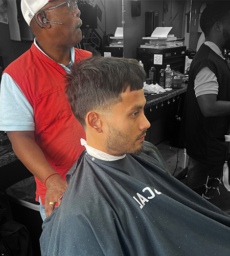 "a picture of a Latino man receiving haircut from barber Roosevelt Williams on the website about page"